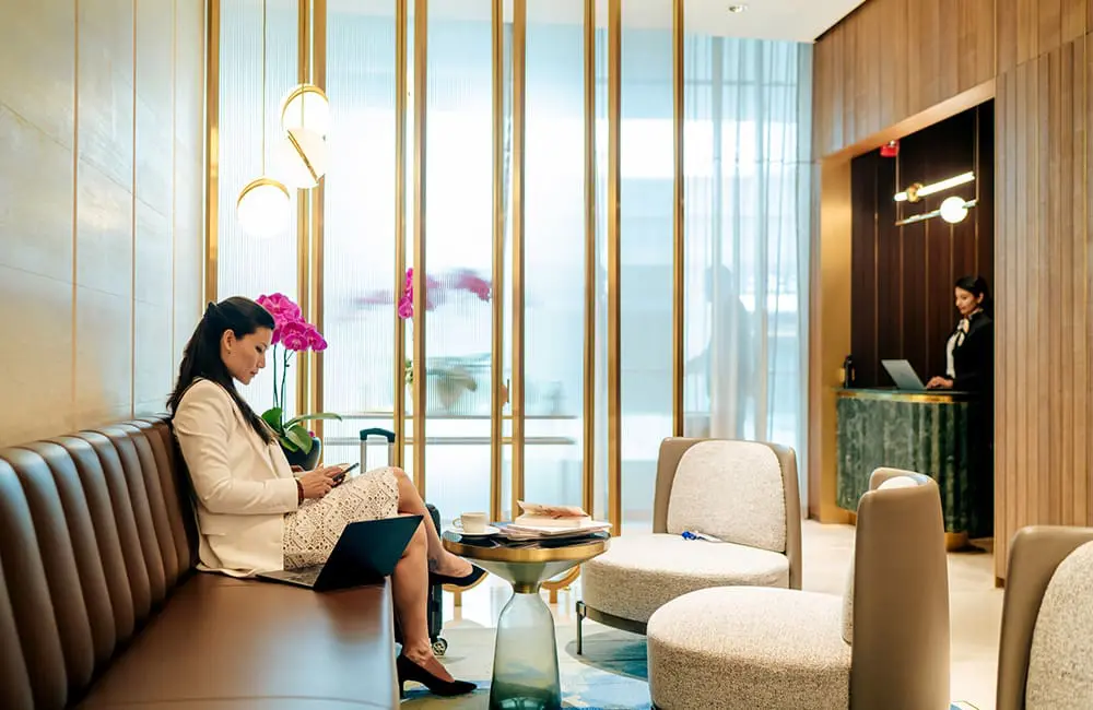 Female traveller with phone and laptop in airport lounges with staff member at counter. Image: Sze kiat Koh/iStock 