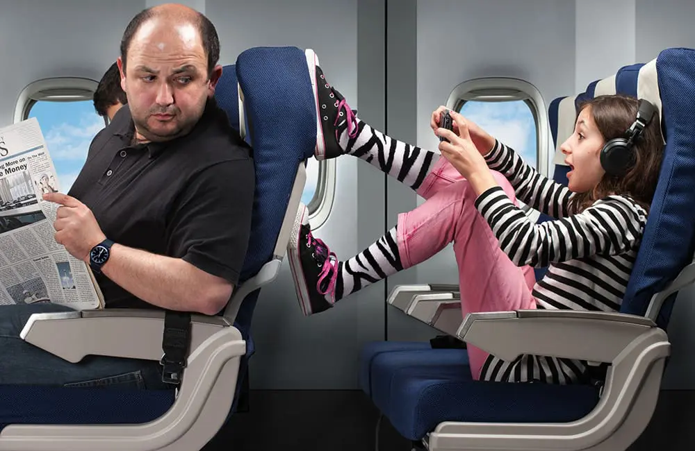 Revealed: The inflight etiquette issue Aussie travellers hate more than anything 1 Girl kicking seat in front on plane while male passenger looks around – inflight etiquette issue. Image: MediaProduction/iStock