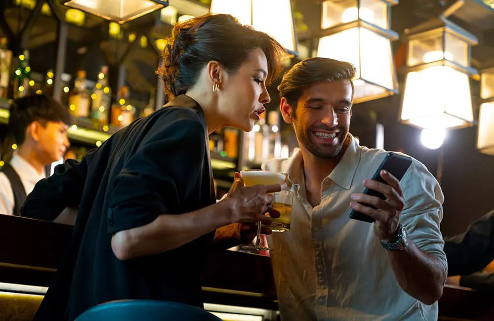 Couple in bar with drinks in Thailand looking at phone. Image: CandyRetriever/iStock