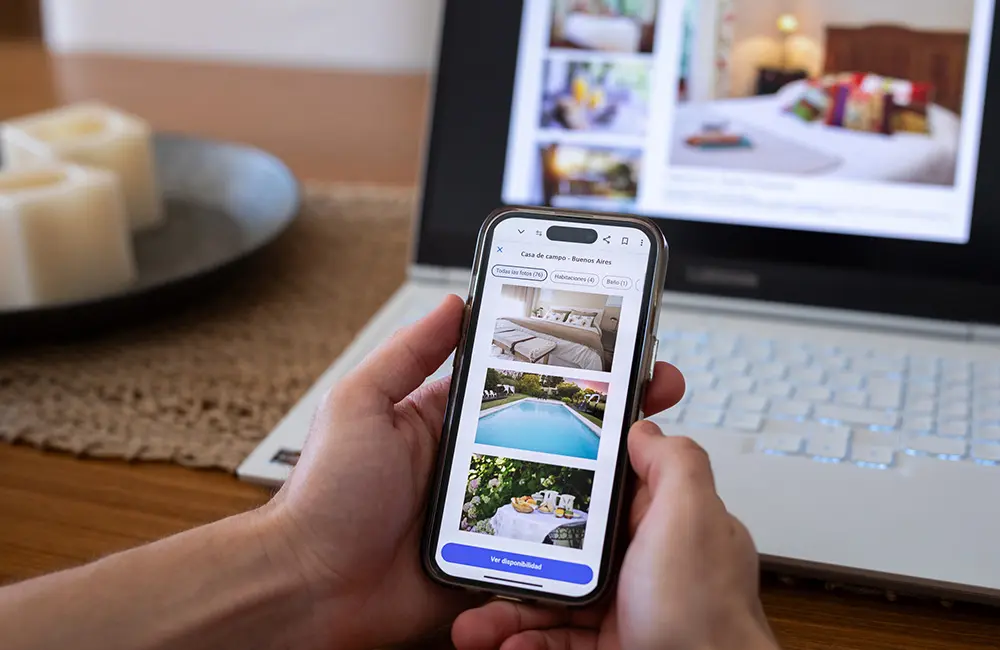 Hands holding smartphone in front of laptop with hotel bookings. Image: ruizluquepaz/iStock