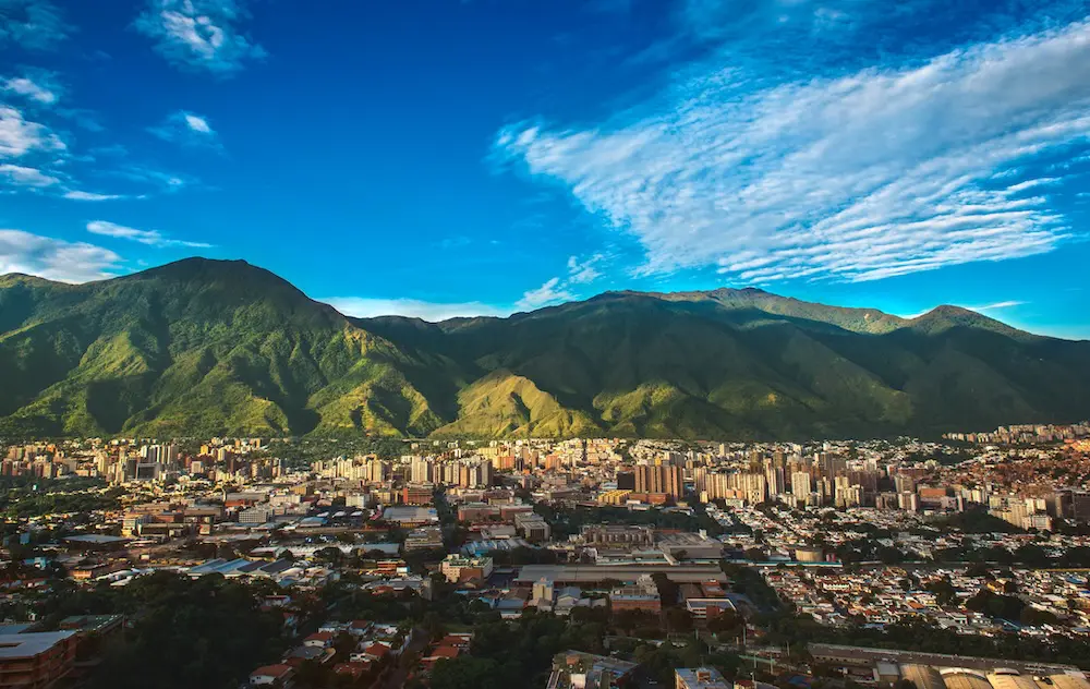 Photograph of Caracas, a Venezuelan city under siege from organized crime and corruption, shot during a beautiful sunny November afternoon displaying the vibrant contrast between the inherent beauty of the city (as shown from a far wide angle shot) and the internal dangers of its daily life. LATAM story