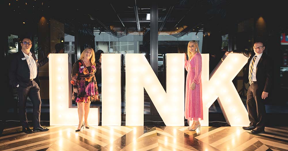 Four people stand around large illuminated letters that spell 'LINK'