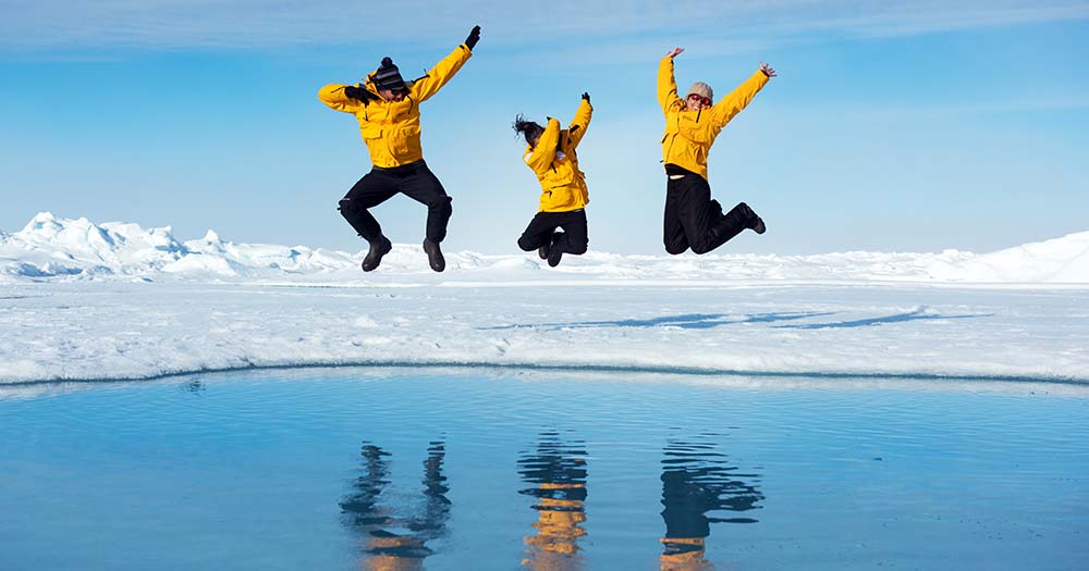Three people jumping in air reflected in water in the Arctic.