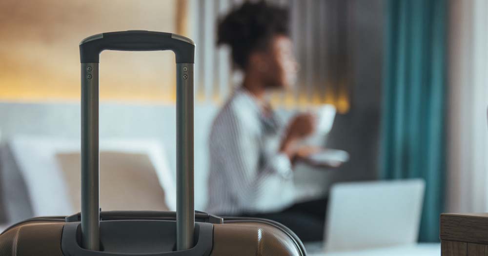Woman drinking tea in hotel room, suitcase in focus