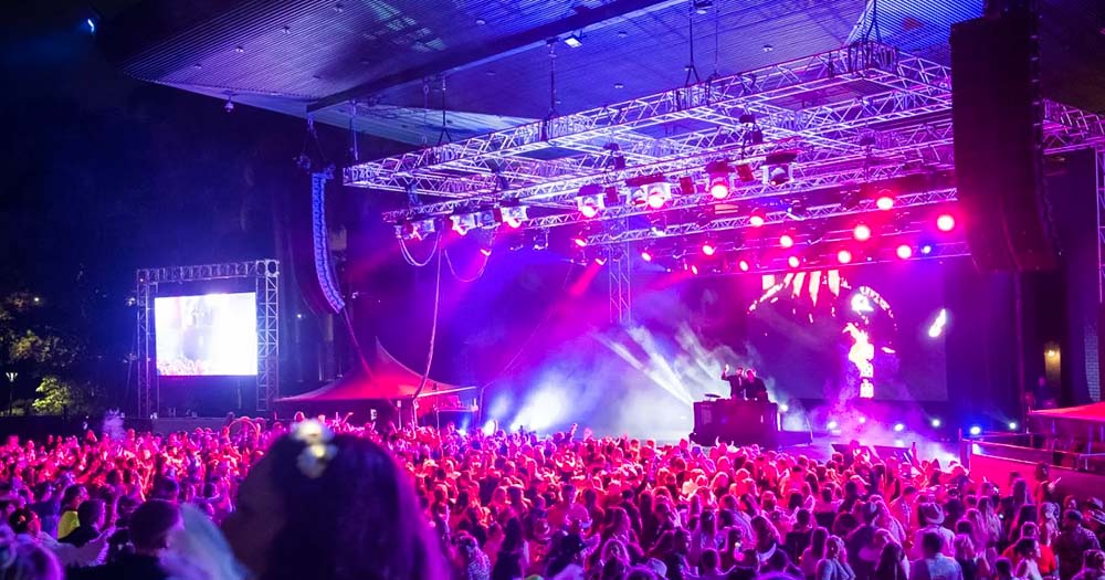 DJs on stage at night at outdoor music festival with coloured lights and lasers.