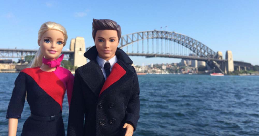 Barbie and Ken dolls in Qantas uniforms against Sydney Harbour Bridge.