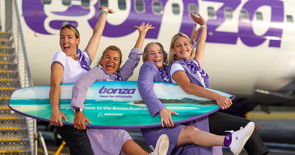 Four female airline crew with surfboard on airport tarmac outside airplane