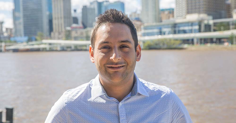 Headshot of man outdoors against Brisbane River and cityscape.