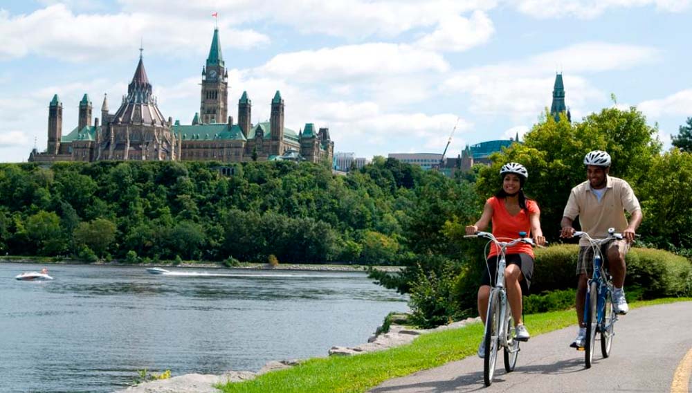 DC Ottawa River Cyclists with Parliament Hill credit Ottawa Tourism