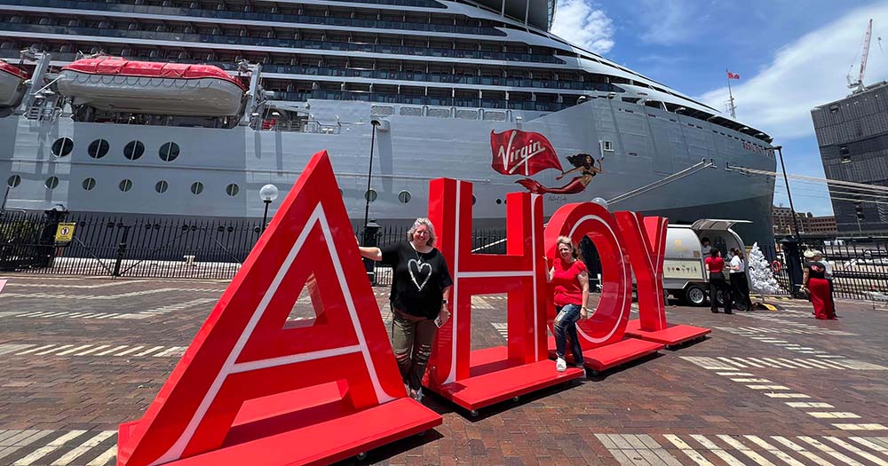 'Ahoy' letters in red in front of Virgin Voyages' Resilient Lady ship