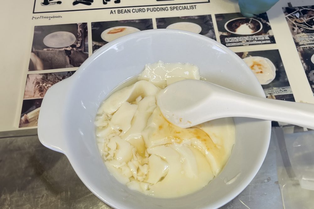 A bowl of white creamy tofu with yellowy-orange ginger syrup drizzled on top.