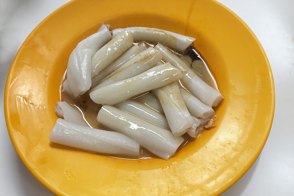 A yellow bowl with long cylinder shaped rice noodles covered in sesame oil and soy sauce.