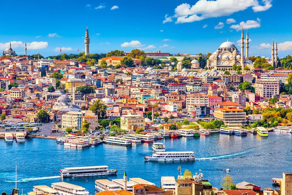 Touristic sightseeing ships in Golden Horn bay of Istanbul and mosque with Sultanahmet district against blue sky and clouds. Turkish Airlines