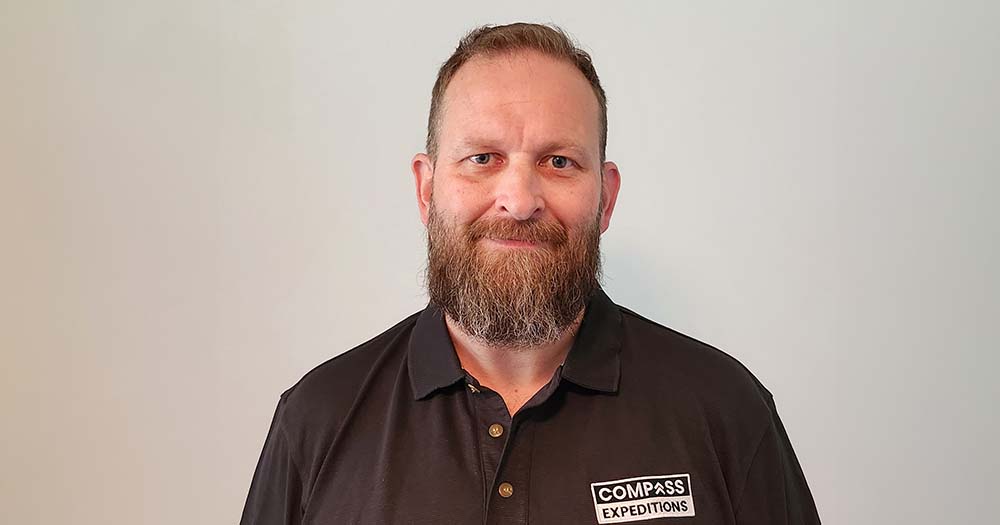 Headshot of bearded man in black polo shirt embroidered with Compass Expeditions against plain background.