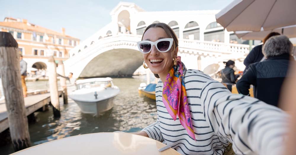 Happy female traveller taking selfie on boat in Venice, Italy.