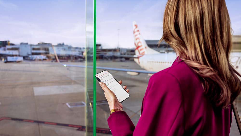 Woman looks at Virgin Australia plane while holding smartphone with app to track baggage.