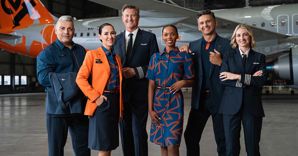 Jetstar pilot, cabin crew and airport staff model the new uniform in aircraft hangar with plane behind.