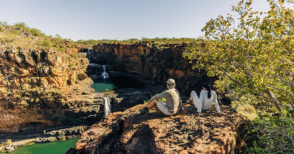 Couple sitting on rock looking at Punamii Uunpuu Mitchell Falls in the Kimberley, WA with Outback Spirit tours.