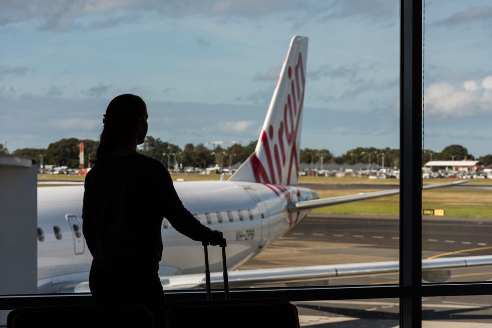 Woman in silhouette at airport gate with Virgin plane tail seen through window