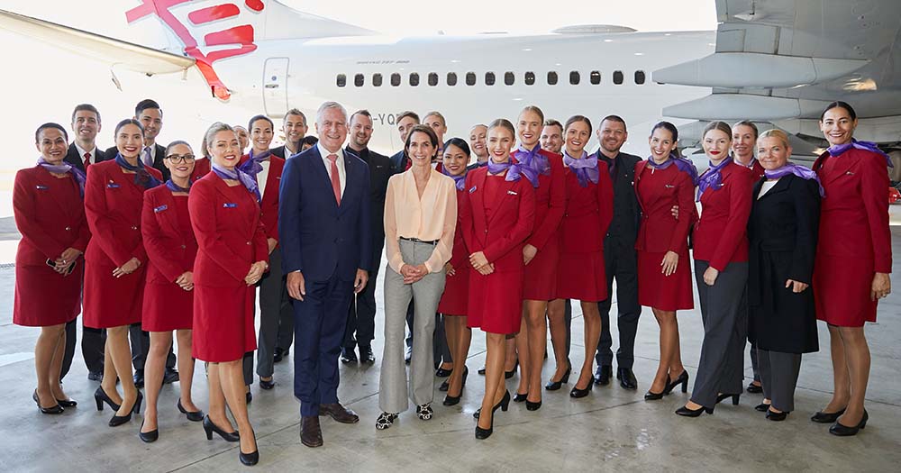 Virgin Australia cabin crew with CEO Jayne Hrdlicka in front of VA plane in hangar.