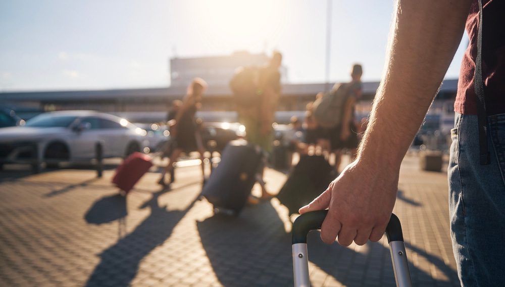 Traveller with suitcase with blurred background of airport and travellers to illustrate UNWTO travel rebound data.