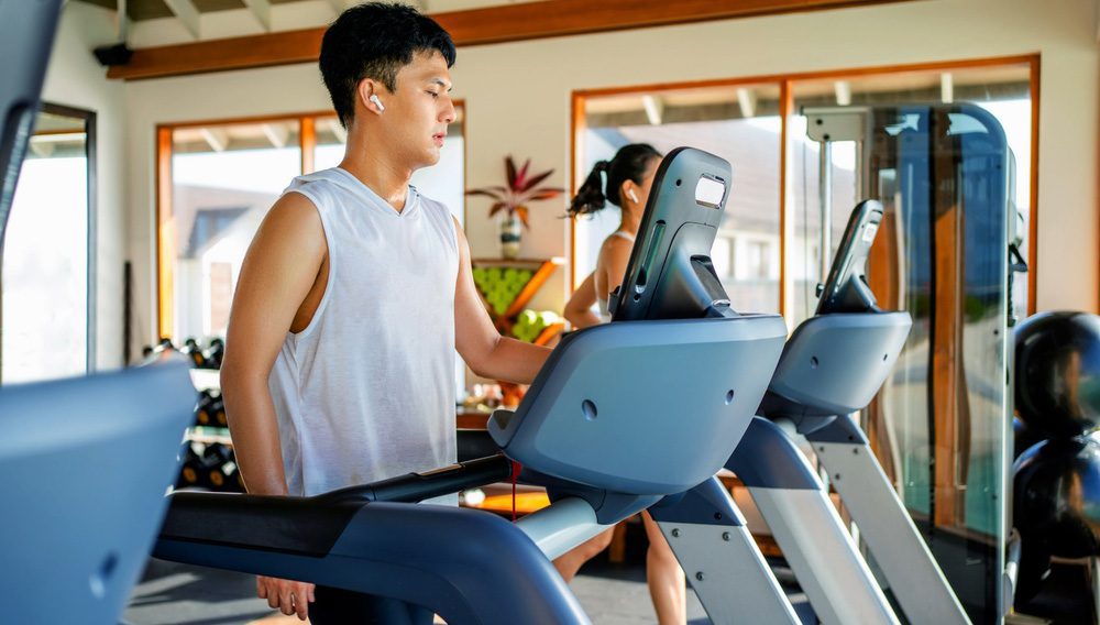 Male and female business travellers on treadmills in hotel gym.