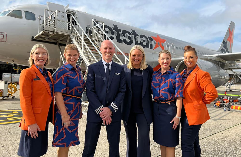 Group of Jetstar employees on tarmac in front of plane.
