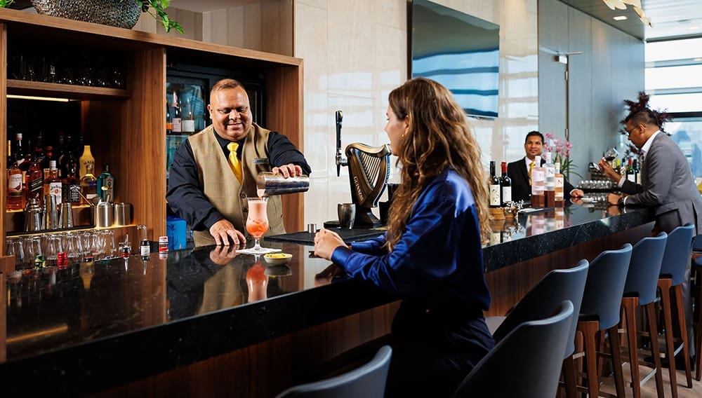 SilverKris Lounge at London Heathrow Business Class Lounge cocktail bar with passengers and bartender pouring drink.