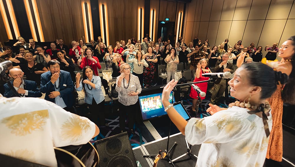 Wide shot of audience learning to do the hula.