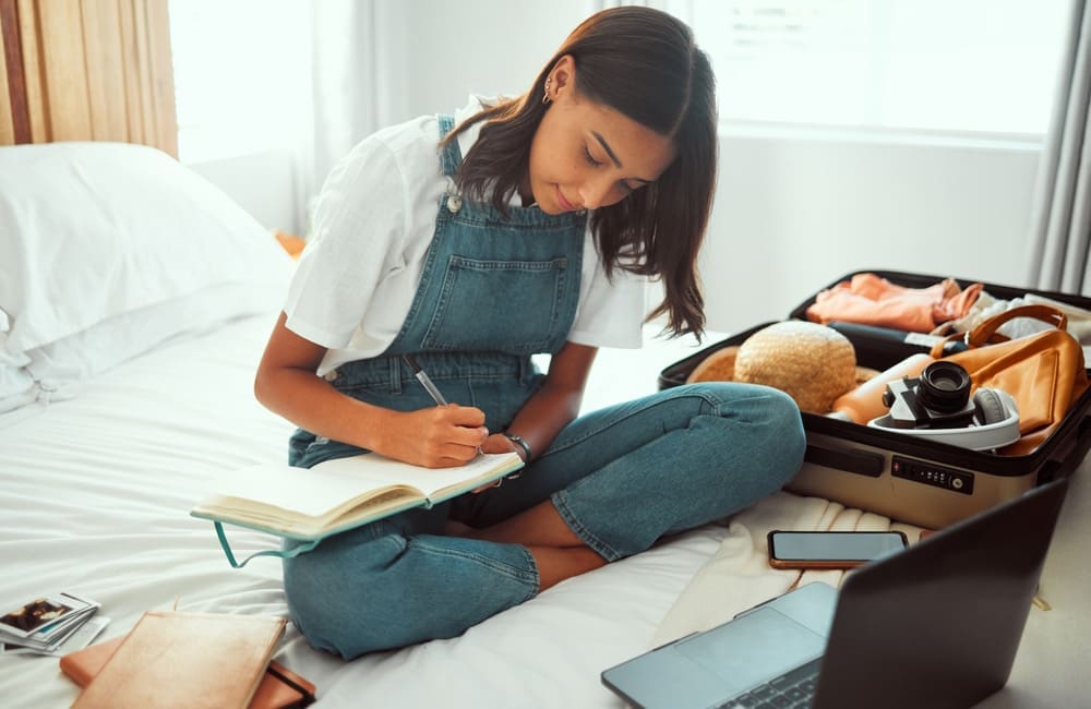 Young woman on bed with suitcase open planning a trip.