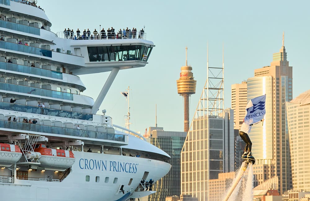 Close-up of person with water jet-pack and Princess Cruises flag outside Crown Princess cruise ship and Sydney CBD buildings.