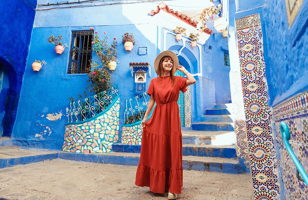 Woman in long dress against blue buildings in Chefchaouen, Morocco.