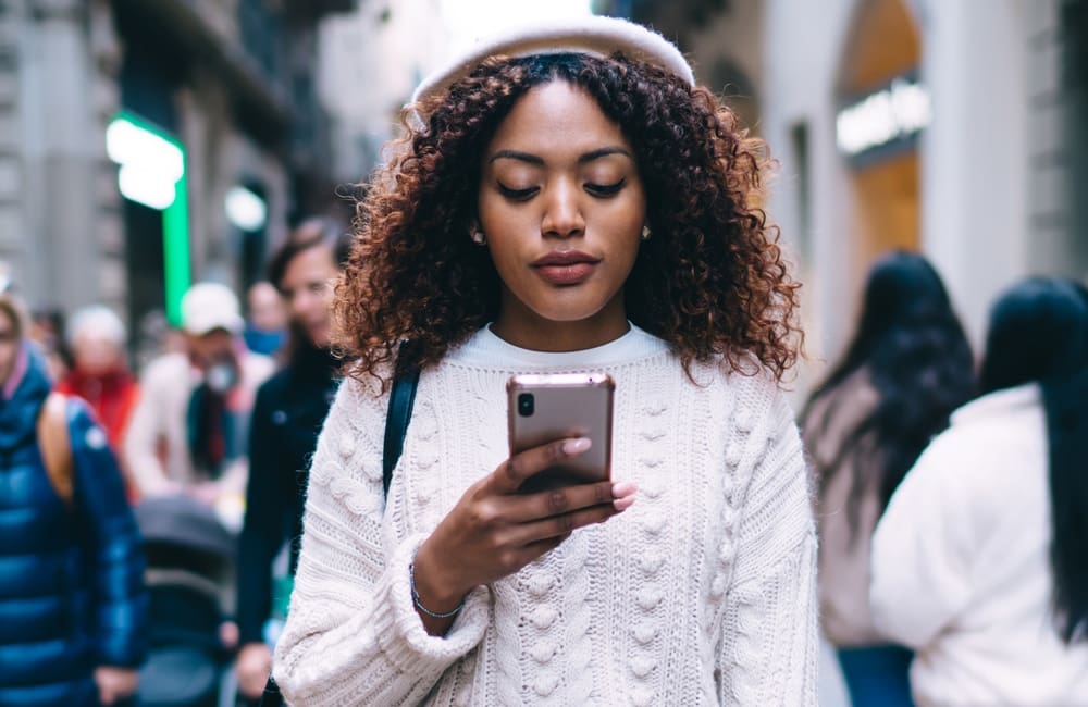 Female traveller in busy city street looking at her mobile phone – international roaming charges concept