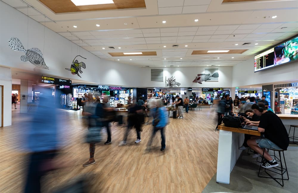 Blurred image of passengers walking and seated in retail area in Cairns Airport.