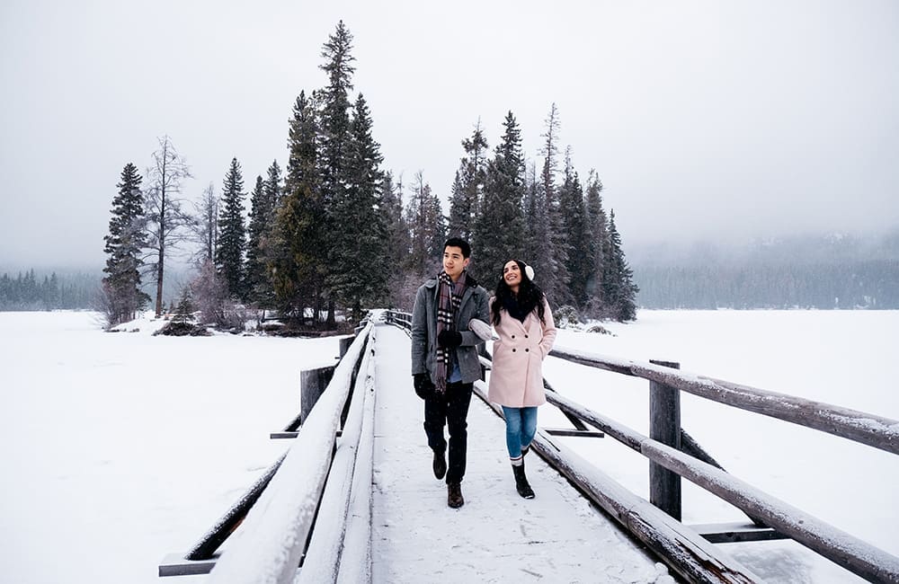 Couple walking on bridge in Jasper National Park in winter.
