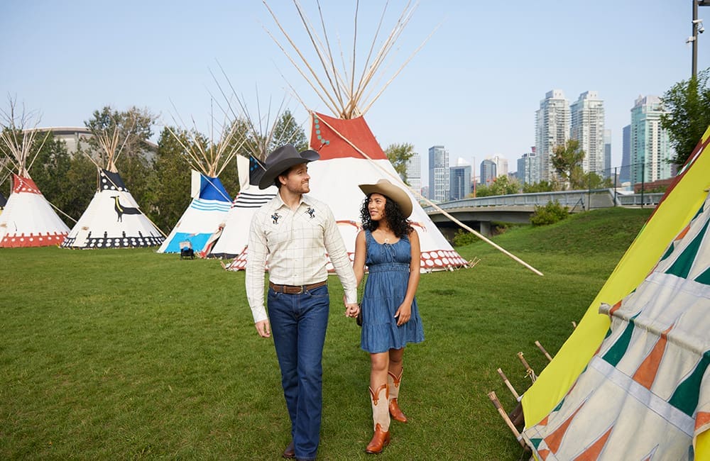 Couple walking among tipis at Elbow River Camp at the Calgary Stampede. Image: Colin Way
