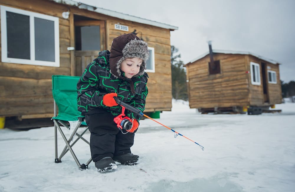 Small child ice fishing outside wooden huts in Ontario. Image: Destination Ontario