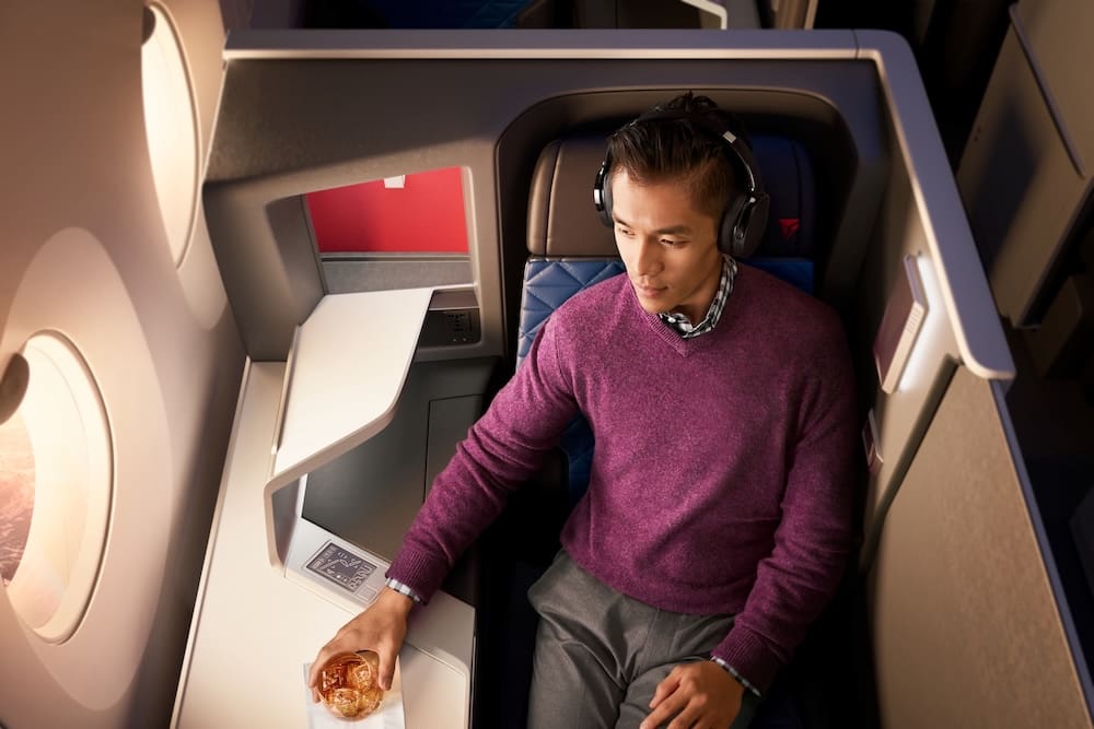 A man in headphones relaxes with a beverage in Delta One suite