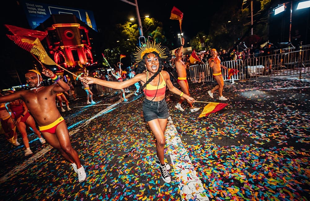 People dressed in lifesaver uniforms with red and yellow flags at the 2024 Sydney Gay & Lesbian Mardi Gras Parade. Image: Jordan Munns