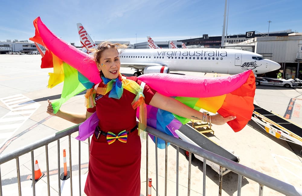 Virgin Australia attendant with rainbow wings and costume in front of Virgin Australia aircraft for Pride Flights.