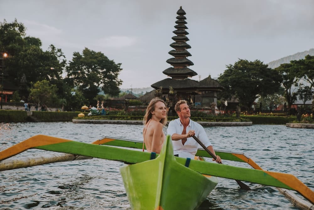 Happy young couple spending time at the ulun datu bratan temple in Bali, cruising on a catamaran
