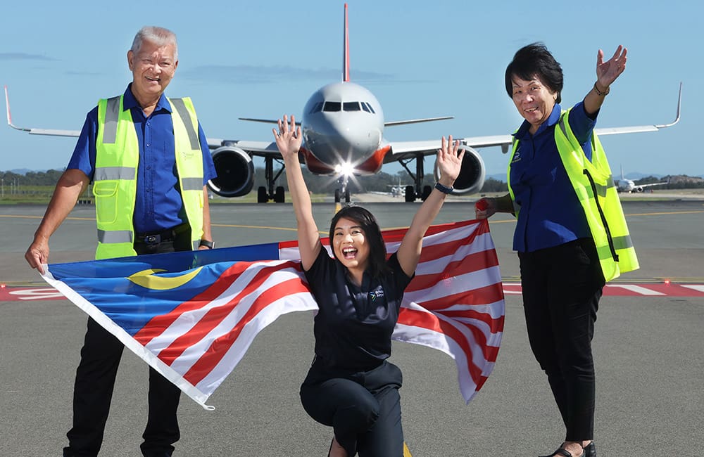 Brisbane Airport staff on tarmac with plane in background and Malaysia flag.