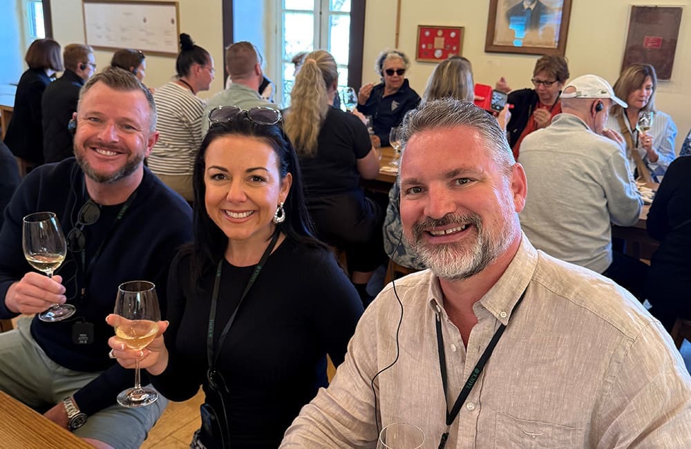 Three people seated with wine glasses at a Douro River Valley wine estate tasting with other people in the background.