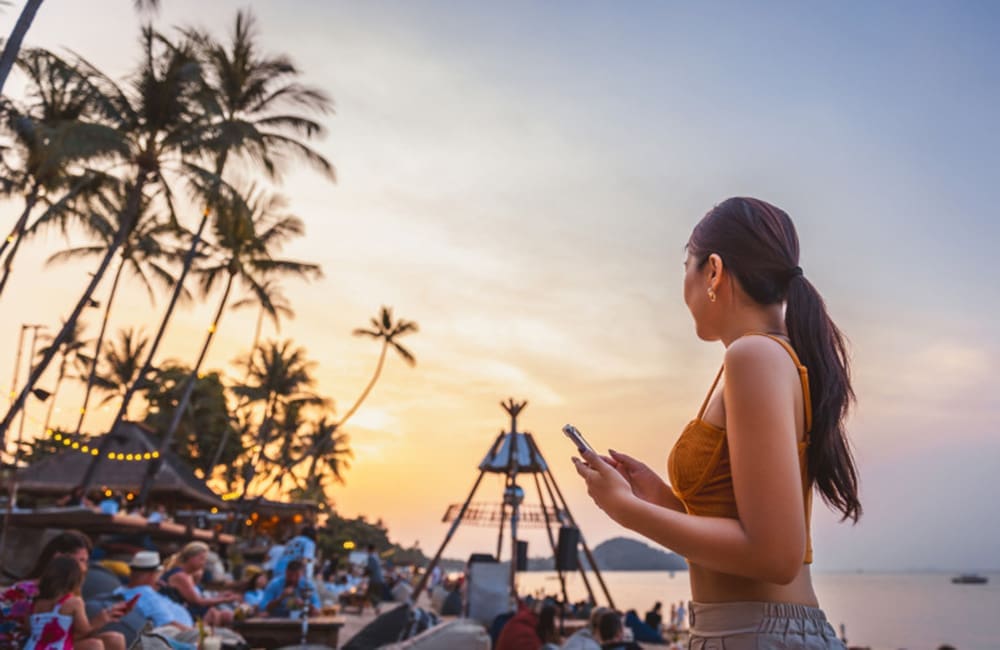 Woman at beach festival holding smartphone – AI travel recommendations