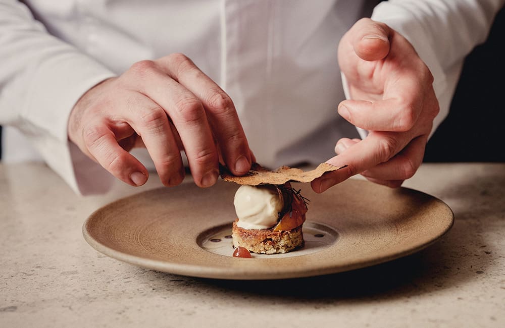 Close-up of chef's hand plating a meal.  Image: Belmond