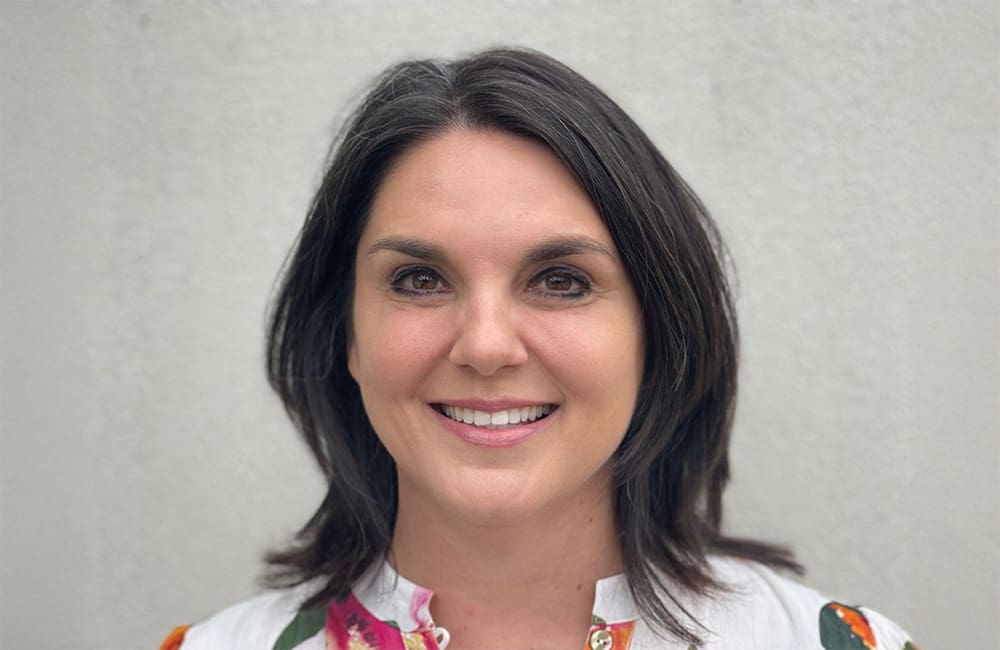 Corporate headshot of woman against plain background.