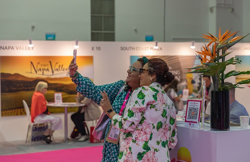 Two women taking a selfie in front of a booth at ILTM Asia Pacific 2025 in Singapore