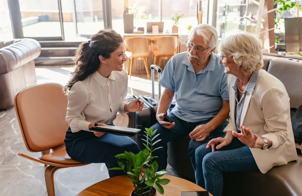 Boomer couple sit with hospitality team member to check-in via tablet – use AI to book holidays
