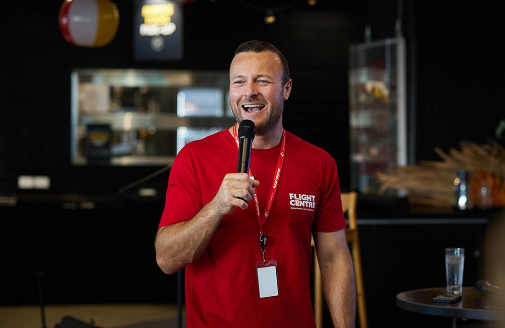 Flight Centre Global MD Andrew Stark in red t-shirt with microphone at event
