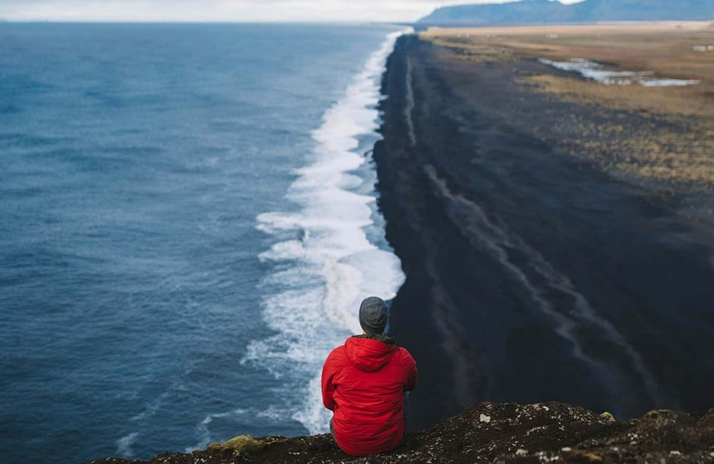 Man sitting on cliff edge looking at sea – Roam by Tauck